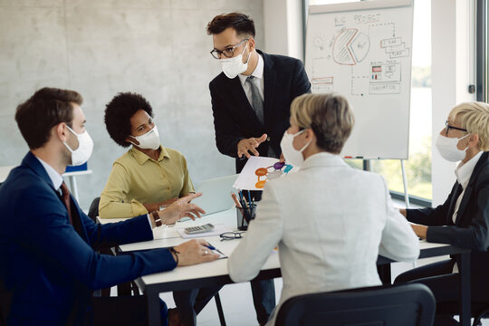 Group of coworkers with face masks analyzing business reports during a meeting in the office.