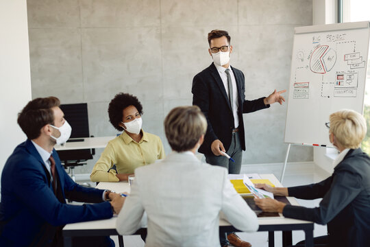 Young businessman with face mask presenting to his coworkers new project on whiteboard in the office. - Powered by Adobe