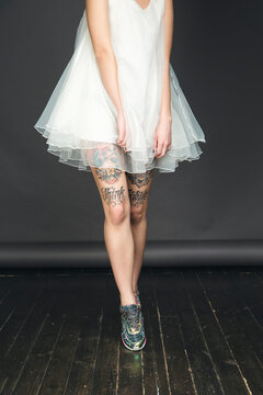 Unrecognizable tattooed female in white dress and trainers