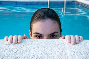 Chica con el pelo mojado por el baño en observando desde el borde de la piscina.