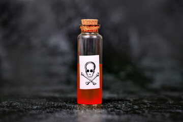 Small vial with cork and red liquid and poison skull label on dark background