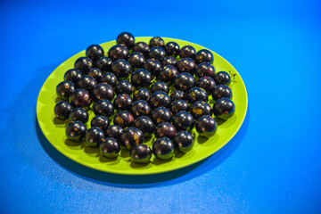 Jaboticaba (Myrciaria cauliflora) fruits in green dish on blue background