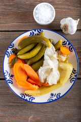 Assorted pickled vegetables in bowl/plate with garlic and salt in bowl on natural wooden background.