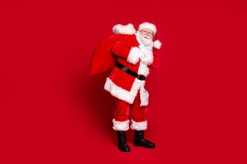 Photo portrait of santa claus carrying large sack of presents isolated on vivid red colored background