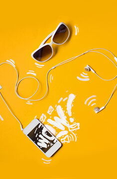 White smartphone and sunglasses with design drawings on yellow background.