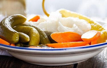 Assorted pickled vegetables in bowl/plate with garlic and salt in bowl on natural wooden background.