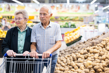 mature spouses chooses potato in vegetable section of supermarket