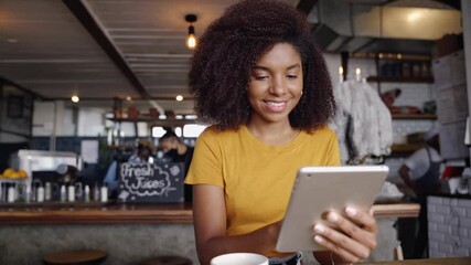 Beautiful smiling woman sitting at trendy cafe scrolling on tablet next to cup of hot coffee.