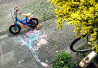 Child's red tricycle parked on a cobble design paved street its shadow painted with chalk - Powered by Adobe