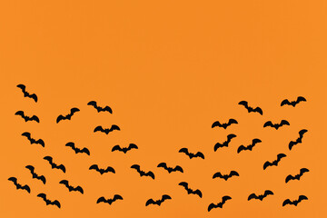 Halloween deco confetti in shape of small flying black bats on orange background with empty copy space