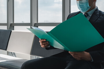 Asian businessman sitting in office space,wearing face mask watching reports from the file.