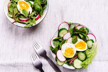 Radish, cucumber, herb mix and soft-boiled egg salad in two bowls on white tablecloth. Healthy nutrition. Selective focus