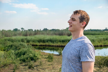 Happy casual man enjoying and relaxing standing in a field with lake in the background