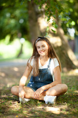 teenager girl in denim overalls sits on the grass, lit by sun bunnies