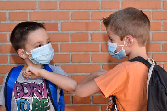 Retrato de dos ni&ntilde;os con mochilas y mascarilla quir&uacute;rgicas salud&aacute;ndose con el codo