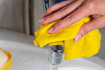 housewife yellow a damp cloth to clean the faucet in the bathroom. Concept of home cleaning and...