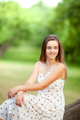 a girl in a light white dress with polka dots sits on a huge old tree