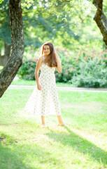 Fototapeta na wymiar beautiful girl in a summer dress stands on a sunny meadow