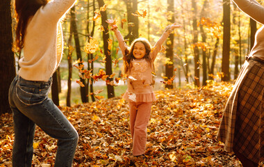 Obraz na płótnie Canvas A beautiful couple of lesbian ladies having fun in the autumn forest with their adopted teenage daughter. The young homosexual family playing with her daughter. 