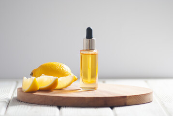 Yellow cosmetic oil and sliced lemon pieces on the light wooden and gray background close-up picture