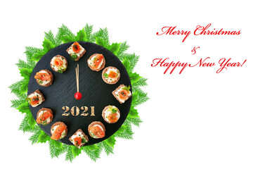 Happy New Year 2021! Smoked salmon canapes on black slate platter form a clock face showing midnight over a fir tree wreath isolated