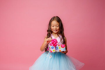 a little girl of Asian appearance holds a gift in her hands celebrating her birthday on a pink background