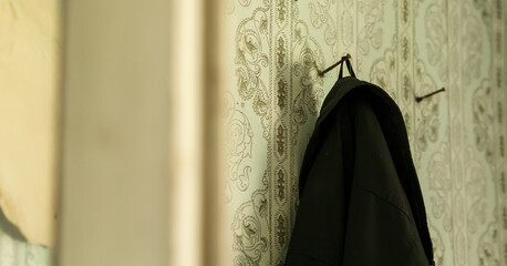 black coat of man hanging on hook or toenail in shabby wall of room in abandoned house