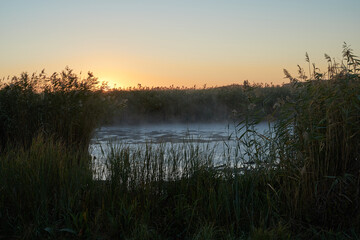 Autumn time. Dawn over the river in a misty, brooding haze. Beautiful view of the forest and river, covered with fog in the early morning. The sun's rays of light. September.