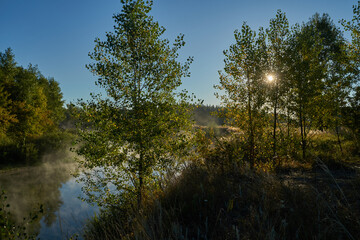 Autumn time. Dawn over the river in a misty, brooding haze. Beautiful view of the forest and river, covered with fog in the early morning. The sun's rays of light. September.