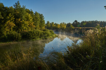 Autumn time. Dawn over the river in a misty, brooding haze. Beautiful view of the forest and river, covered with fog in the early morning. The sun's rays of light. September.