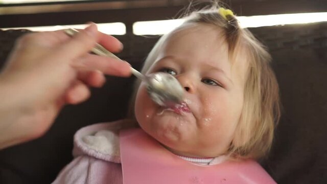 Little chubby baby girl hilariously open mouth full of milk food eating very good appetite feeding from spoon