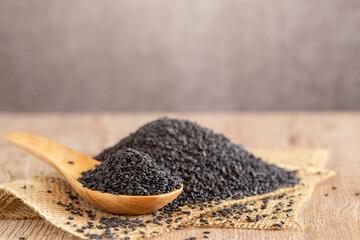 Black dried sesame seed on wooden spoon over wood table.