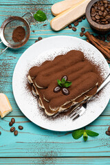 Two portions of Classic tiramisu dessert on ceramic plate and savoiardi cookies on colorful blue wooden background
