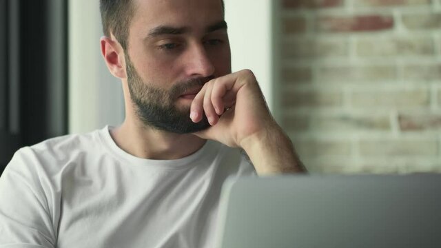 Young serious man using laptop computer indoors at home