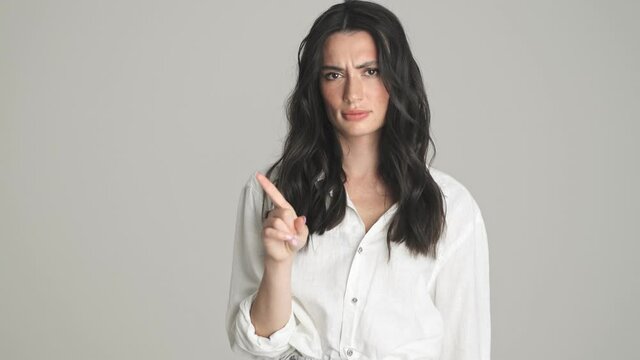 A serious young woman is shaking her finger negatively standing isolated over gray background