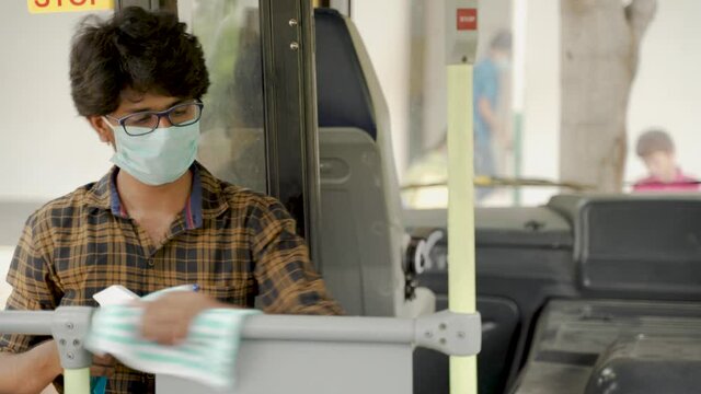 Young man in medical mask disinfecting or sanitizing bus handlebars by using alcohol Disinfectant spray to protect people from coronavirus or covid-19 infection.