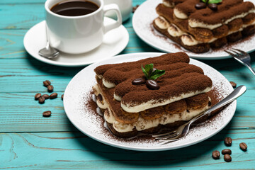 Two portions of Classic tiramisu dessert, cup of coffee and milk or cream on colorful blue wooden background