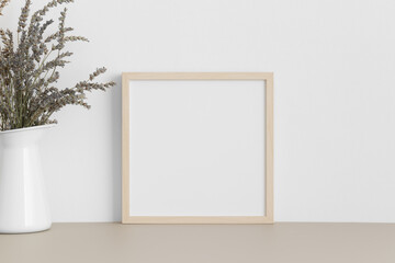 Square wooden frame mockup with a lavender in a vase on a beige table.