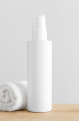 Obraz na płótnie Canvas White cosmetic lotion bottle mockup with a towel on a wooden table.