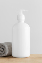 Obraz na płótnie Canvas White cosmetic liquid soap dispenser bottle mockup with a towel on a wooden table.