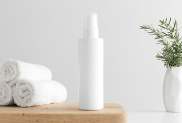 Obraz na płótnie Canvas White cosmetics lotion bottle mockup with towels and a rosemary on a wooden table.