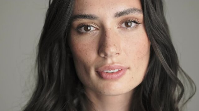 A close-up view of an attractive young woman is smiling to the camera standing isolated over gray background