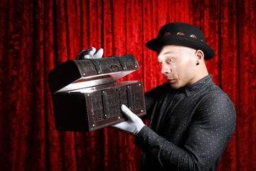 Funny young man in bowler hat and white gloves open treasure chest with gold shining on his face at...