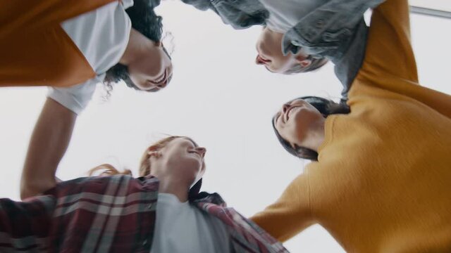 Group of female friends in a huddle and jumping. Low angle view of cheerful females enjoying outdoors.
