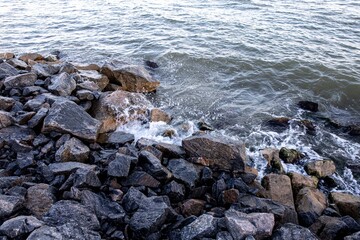 stone and sand seashore with waves in the sunset light