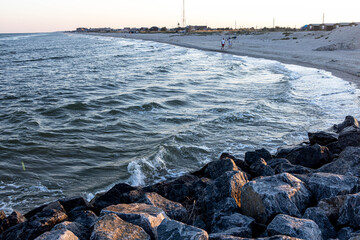 stone and sand seashore with waves in the sunset light