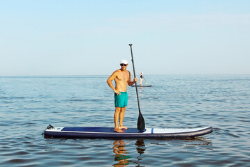 Man is training on a SUP board in the blue sea.