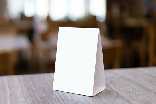 Mock up Label the blank menu frame in Bar restaurant. Stand for booklet with white sheet paper acrylic tent card on table wiht blurred background can inserting the text or picture