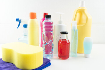 Plastic bottles of cleaning products set with pile clothes on table background.