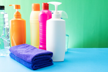 Plastic bottles of cleaning products set with pile clothes on table background.